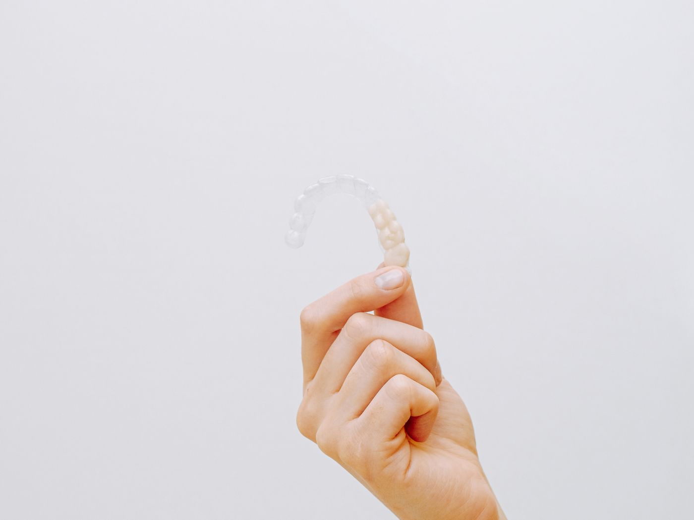 Clear orthodontic aligner tray held in a gloved hand beside a dental arch model