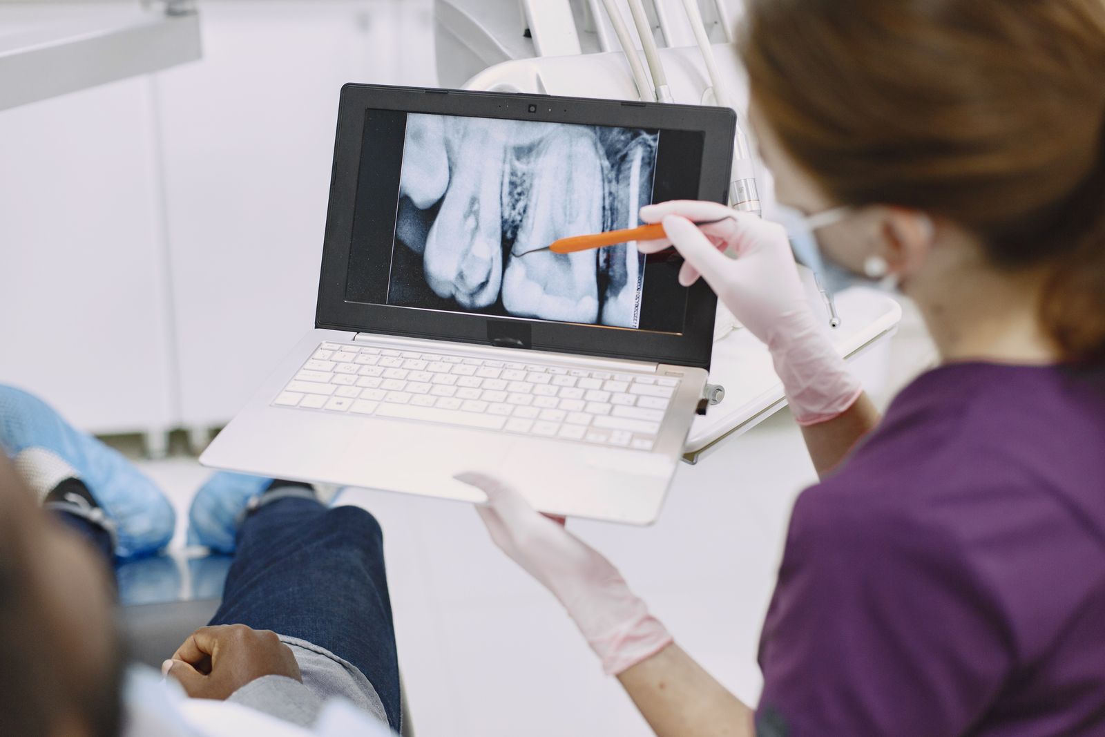 Dentist explaining a dental X-ray and treatment plan to a patient on a laptop